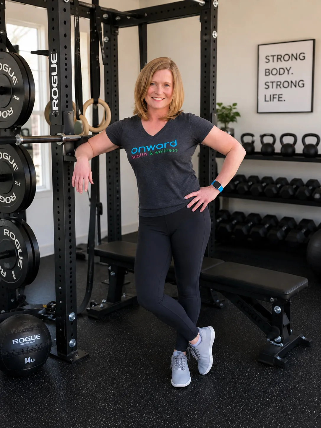 Ann Bolton in her training space, beside a squat rack, kettlebells and dumbbells.